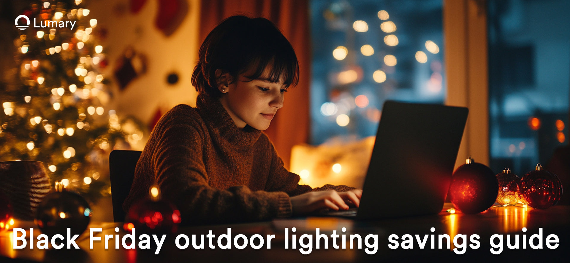 A child sits at a table using a laptop, with a decorated Christmas tree and festive lights in the background.